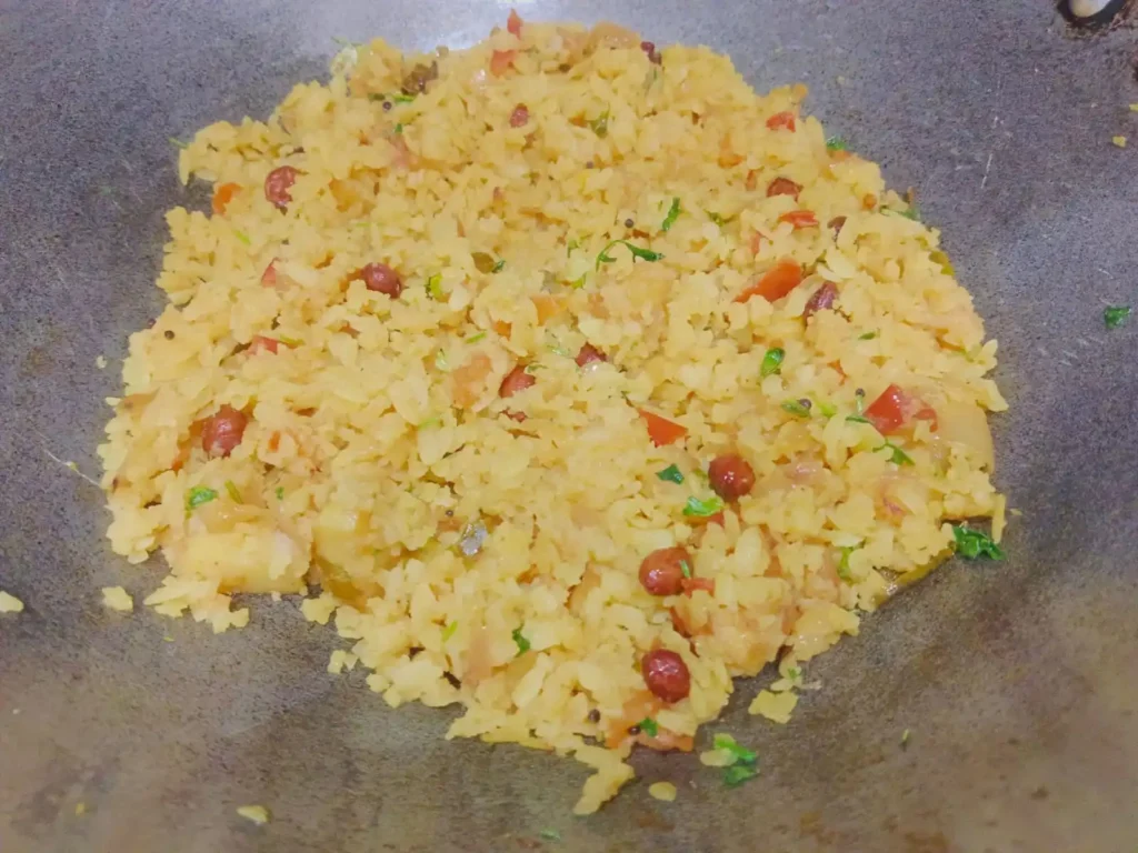 Add the softened poha to the pan and mix gently so the flakes do not break. Cover the pan and cook for 2–3 minutes on low flame until the masala coats the poha evenly.