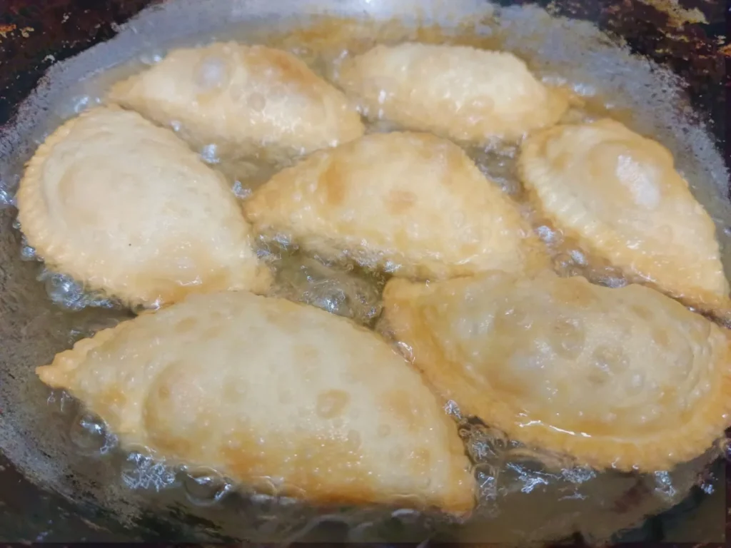 3. In a deep frying pan, heat about 4-5 cups of refining oil over a medium low heat. And once the oil is hot, gently, place the prepared gujiya into the hot oil and fry them on a medium low heat until golden brown and crispy. Do not fry gujiya on a high heat.