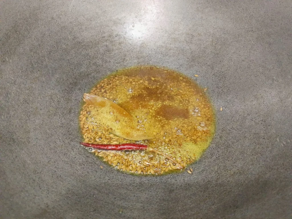 Meanwhile, heat oil in the kadhai and add cumin seeds, dry red chili, and bay leaves. When the mixture begins to smell, also add turmeric and red chili powder.